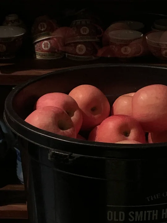 Red apples in a dark bucket with patterned bowls behind them.
