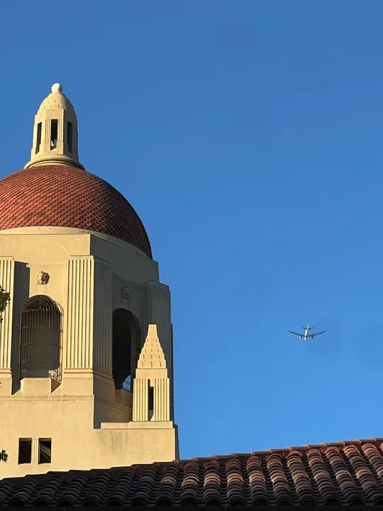 A sunlit tiled dome and a small airplane against a blue sky.