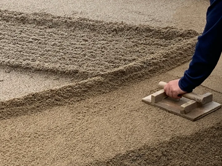 A hand drawing patterns in sand with a wooden tool.